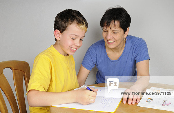 Junge macht Hausaufgaben für die Schule  Mutter unterstützt ihn dabei  beide lachen