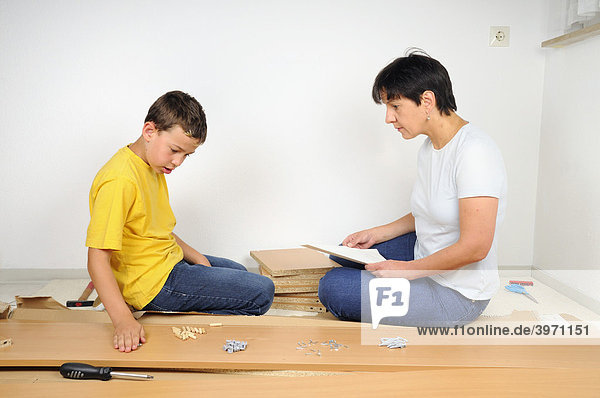 Mutter und Sohn beim Möbel zusammenbauen  Lesen der Anleitung