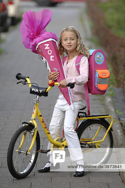 Six-year-old girl with first-day-of-school-cornet on her bike