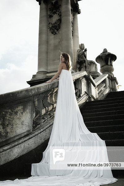 Fashionaufnahme einer jungen dunkelblonden Frau im weißen Kleid mit langer Schleppe angelehnt an das Geländer der Alexanderbrücke  Paris  Frankreich  Europa