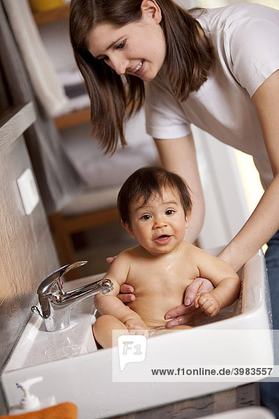 Mother is bathing her nine-month-old baby in the sink