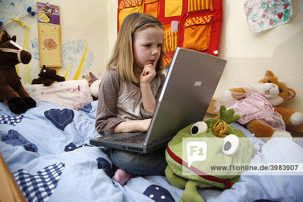 Girl  7 years old  working with a computer at home in her room  sitting on her bunk bed  doing homework for school  educational software