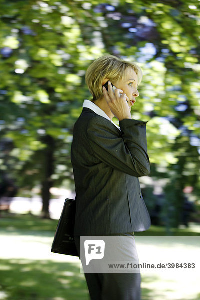 Woman wearing a ladies' suit  trouser suit  businesswoman  early 40s  on her mobile  outdoors  carrying a laptop