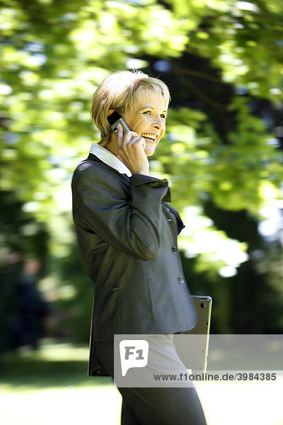 Woman wearing a ladies' suit  trouser suit  businesswoman  early 40s  on her mobile  outdoors  carrying a laptop