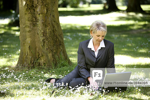 Woman wearing a ladies' suit  trouser suit  businesswoman  early 40s  working on her laptop in a park