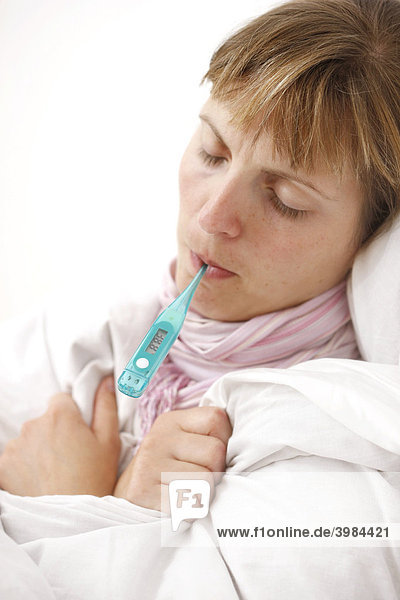 Junge Frau  krank im Bett  mit Fieber  misst die Körpertemperatur mit einem digitalen Fieberthermometer
