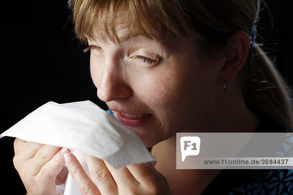 Junge Frau hat Schnupfen  muss niesen  putzt sich die Nase mit einem Papiertaschentuch