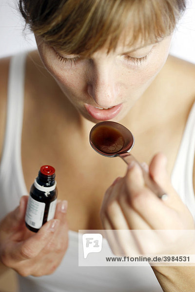 Young woman taking liquid medicine with a spoon  against a cold or cough  stomach drops
