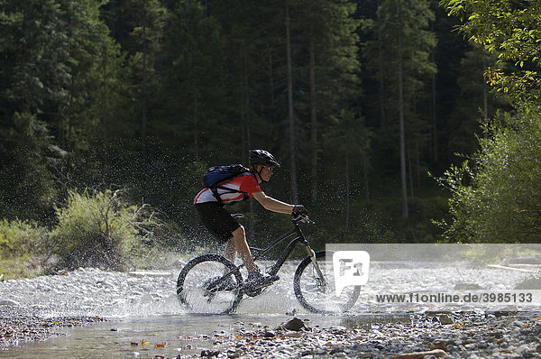 Mountainbike rider riding through a creek in Eschenlainetal valley  Eschenlohe  Upper Bavaria  Bavaria  Germany  Europe