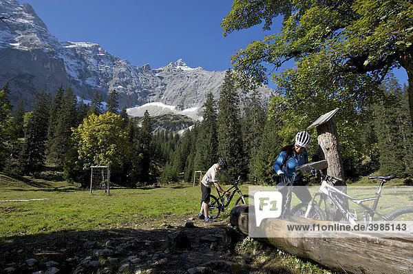 Mountainbike riders  male and female resting at a well  she is filling up her bike bottle  Kleiner Ahornboden forest district  Hinterriss  Tyrol  Austria  Europe