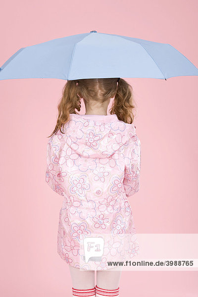 Rothaariges Mädchen mit hellblauem Regenschirm und Regenmantel vor Rosa