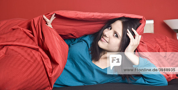 Junge Frau unter roter Bettdecke