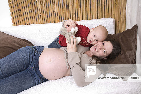 Schwangere Frau spielt mit Kleinkind auf Sofa