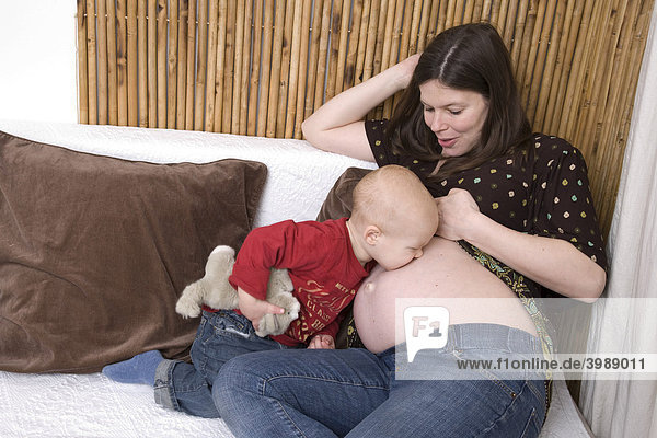Kleinkind küsst seine schwangere Mutter auf den Bauch