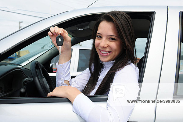 Lächelnde Frau am Steuer ihres Autos zeigt Autoschlüssel