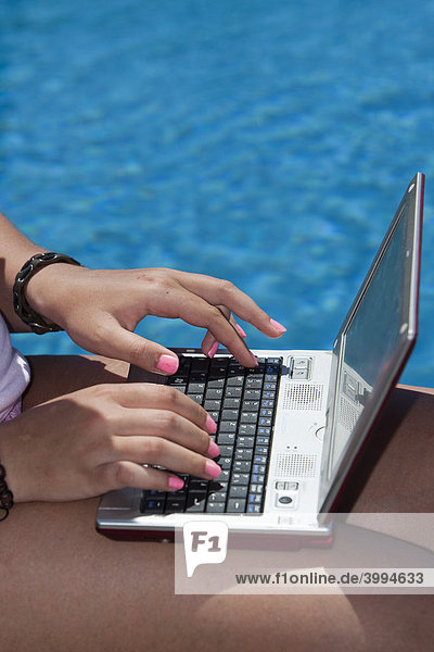 Junge Frau mit Computer am Pool