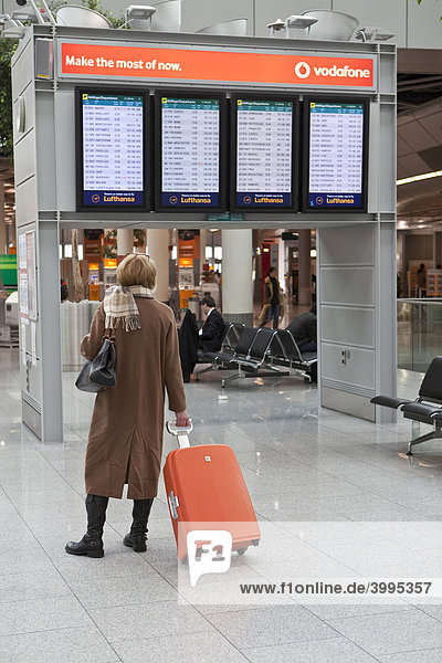 Elegante Frau mit Handgepäck studiert die Abflugzeiten an einer elektronischen Anzeigetafel in der Abflughalle am Flughafen Düsseldorf  Düsseldorf  Nordrhein-Westfalen  Deutschland  Europa