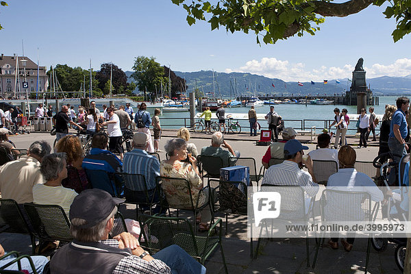 Rentner sitzen an der Uferpromenade von Lindau und hören einem Musikanten zu  Lindau am Bodensee  Bayern  Deutschland  Europa