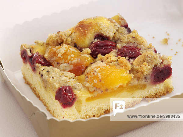 Slice of cake with apricots  cherries and crumbles on a white paper plate