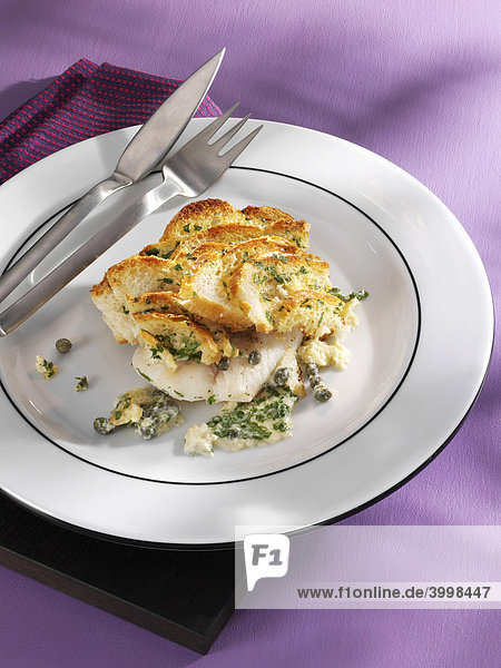 Fish fillet gratin with capers and fish cutlery on a wooden board