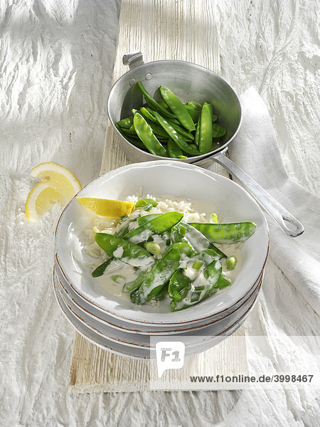Snow peas with lemon sauce and lemon slices for squeezing in a stack of earthenware dishes