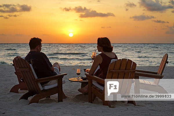 Paar auf Stühlen am Strand mit Longdrink vor untergehender Sonne  Meer  Rihiveli  Insel  Malediven  Süd Male Atoll  Archipel  Indischer Ozean  Asien
