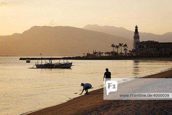 People walking on the beach in the evening  lighthouse  boat  banka  palm trees  romantic mood  Olongapo City  Subic Bay  Luzon island  Philippines  South China Sea  Pacific Ocean