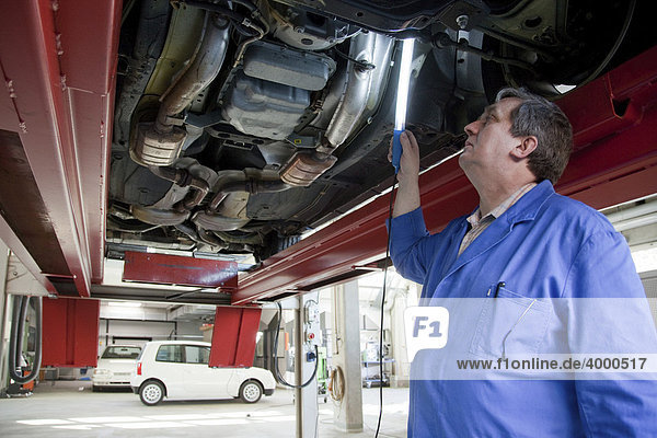 Master Craftsman of motor vehicle mechanics inspecting a car from below in a workshop