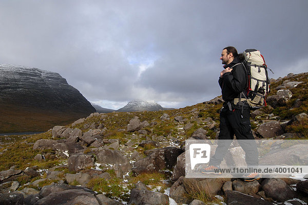 Hiker with hiking backpack on mountain trail in front of a snowy peak  Liathach  Torridon  Scotland  United Kingdom  Europe