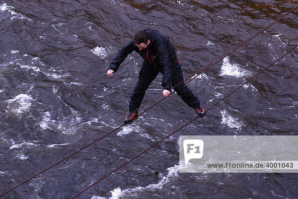 Adventurous hiker crossing over the wire ropes of a drawbridge  rope bridge in Glen Etive  Scotland  United Kingdom  Europe