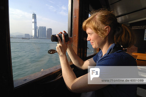 Rothaarige Frau filmt aus der Star Ferry den Blick auf die Skyline von Hongkong Kowloon  Hongkong  China  Asien