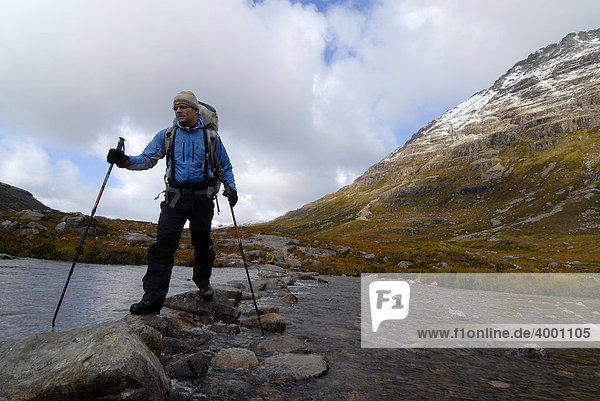 Wanderer mit Trekkingstöcken und Rucksack unterwegs in der schottischen Bergwelt bei einer Flussüberquerung  schottische Highlands  Stuca`Choire Dhuibh Beig  Liathach  Torridon  Schottland  Europa
