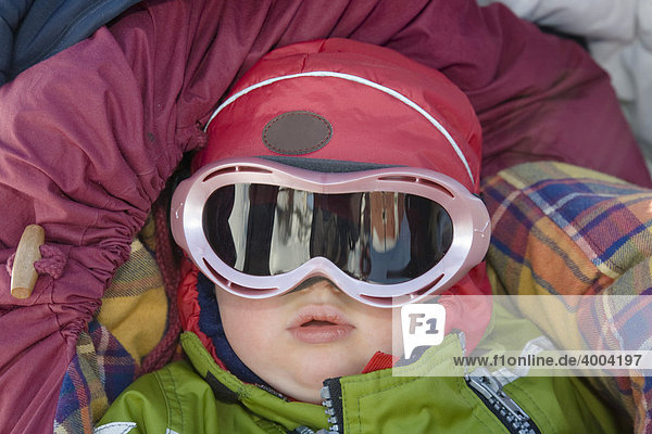 Ein einjähriges Mädchen mit einer Skibrille vor den Augen liegt gut gegen Kälte geschützt im Kinderwagen in Kiruna  Lappland  Nord-Schweden  Schweden