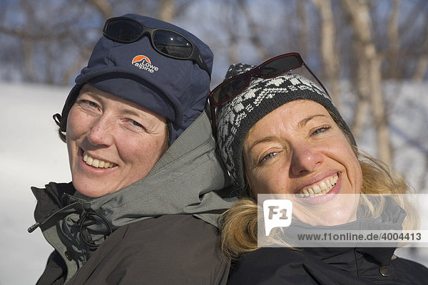 Zwei Frauen sitzen gut gelaunt Rücken an Rücken im Schnee in Kiruna  Lappland  Nord-Schweden  Schweden