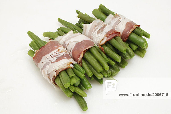 Cooked green beans being wrapped in bacon