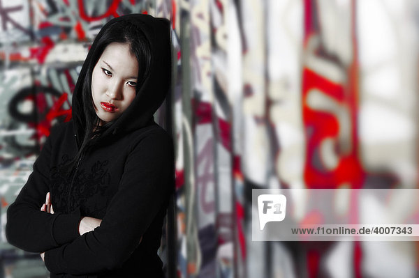 Junges asiatisches Mädchen im Rapper-Stil vor Graffiti-Wand