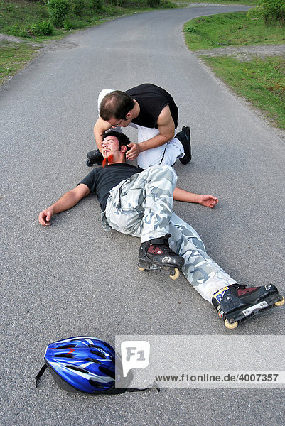 Erste Hilfe  Skater liegt nach Sturz bewegungslos auf der Straße  ein Helfer kümmert sich um ihn