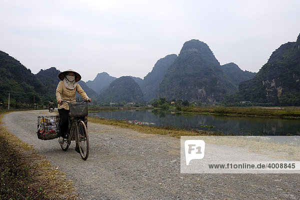 Vietnamese woman on bicycle collecting trash in front of karst mountains  National Park TamCoc  Ninh Binh  North Vietnam  South East Asia