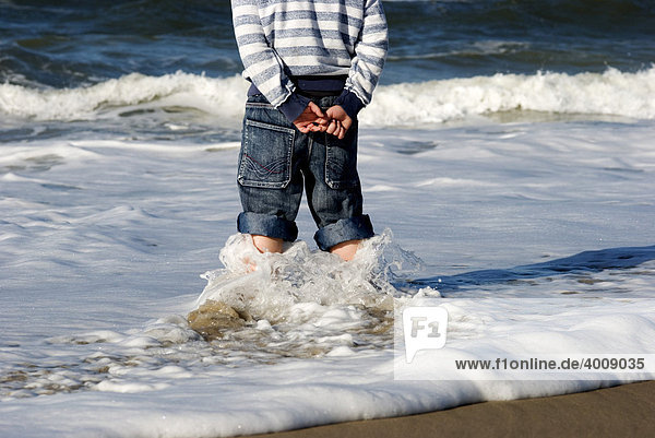 Junge steht in einer Welle an der Nordseeküste von Holmesland  Jütland  Dänemark  Europa