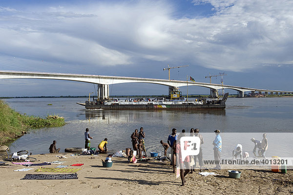 People washing clothes and bathing at the Zambezi riverbank the new Zambezi bridge at back Caia Mozambique Africa