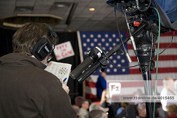A television camera operator doing a crossword puzzle in a newspaper while waiting for the beginning of a John McCain presidential campaign rally  Warren  Michigan  USA