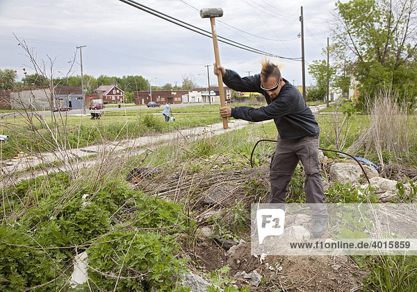 Ein Mann zerkleinert alte Betonblöcke für die Ränder von erhöhten Beeten in einem Stadtgarten  der auf einem leerstehenden Grundstück in einem armen Stadtteil eingerichtet wird  Detroit  Michigan  USA