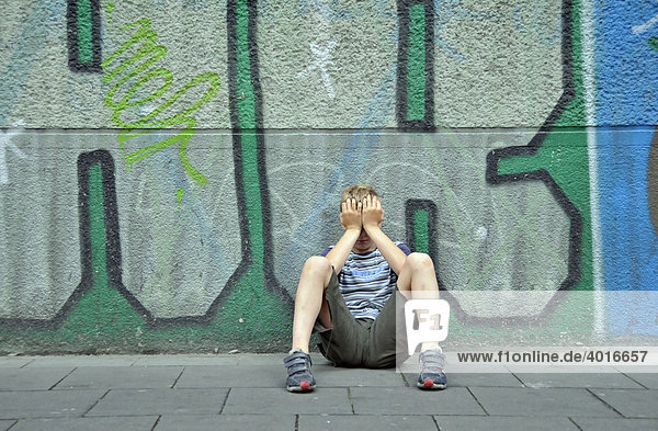Frustrierter neunjähriger Junge vor einer Graffitiwand  Deutschland  Europa