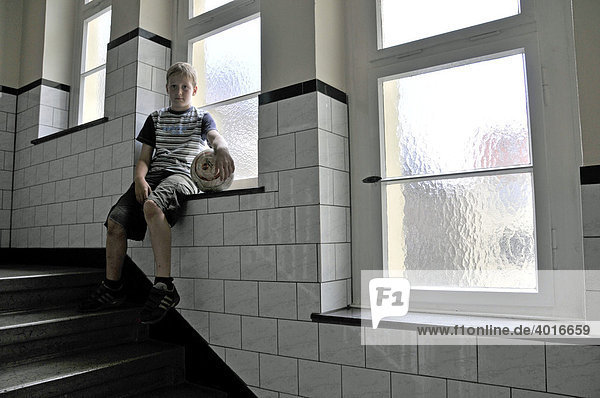 Lonely nine-year-old boy with football in the hallway  Germany  Europe