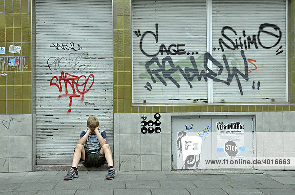 Einsamer neunjähriger Junge vor einem geschlossenen und mit Graffiti verschmierten Geschäft  Deutschland  Europa