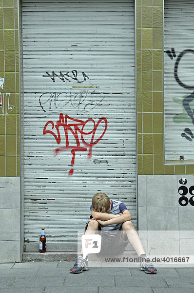 Einsamer neunjähriger Junge vor einem geschlossenen und mit Graffiti verschmierten Geschäft  Deutschland  Europa