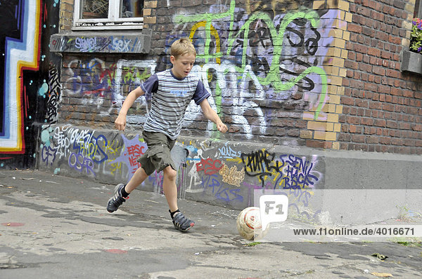 Ein neunjähriger Junge spielt mit seinem Fußball vor einer Graffitiwand  Bolzplatz in Köln  Nordrhein-Westfalen  Deutschland  Europa