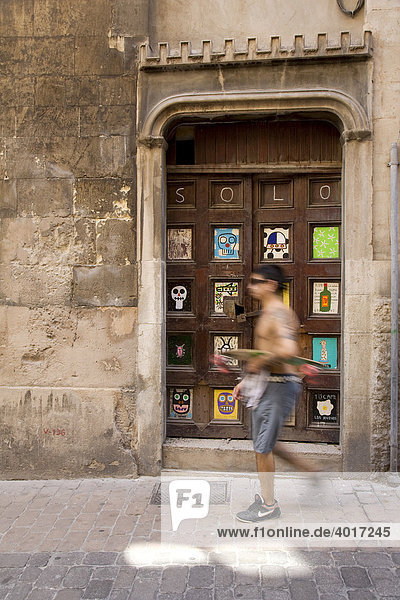 Spanish man with a skateboard in front of a door with artwork by Albert Pinya  Calle Sant Feliu  Palma de Mallorca  Majorca  Balearic Islands  Spain  Europe