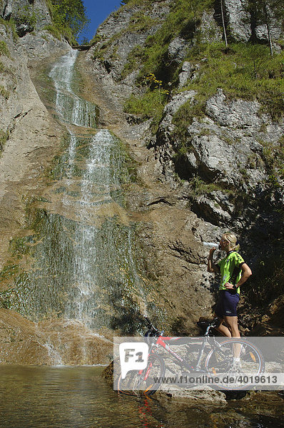 Frau  22 Jahre  mit Mountainbike und Raddress steht an einem Wasserfall  Nationalpark Kalkalpen  Oberösterreich  Österreich  Europa