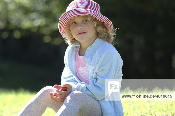 Lächelndes Mädchen  5 Jahre  mit Hut im Gegenlicht  sitzend